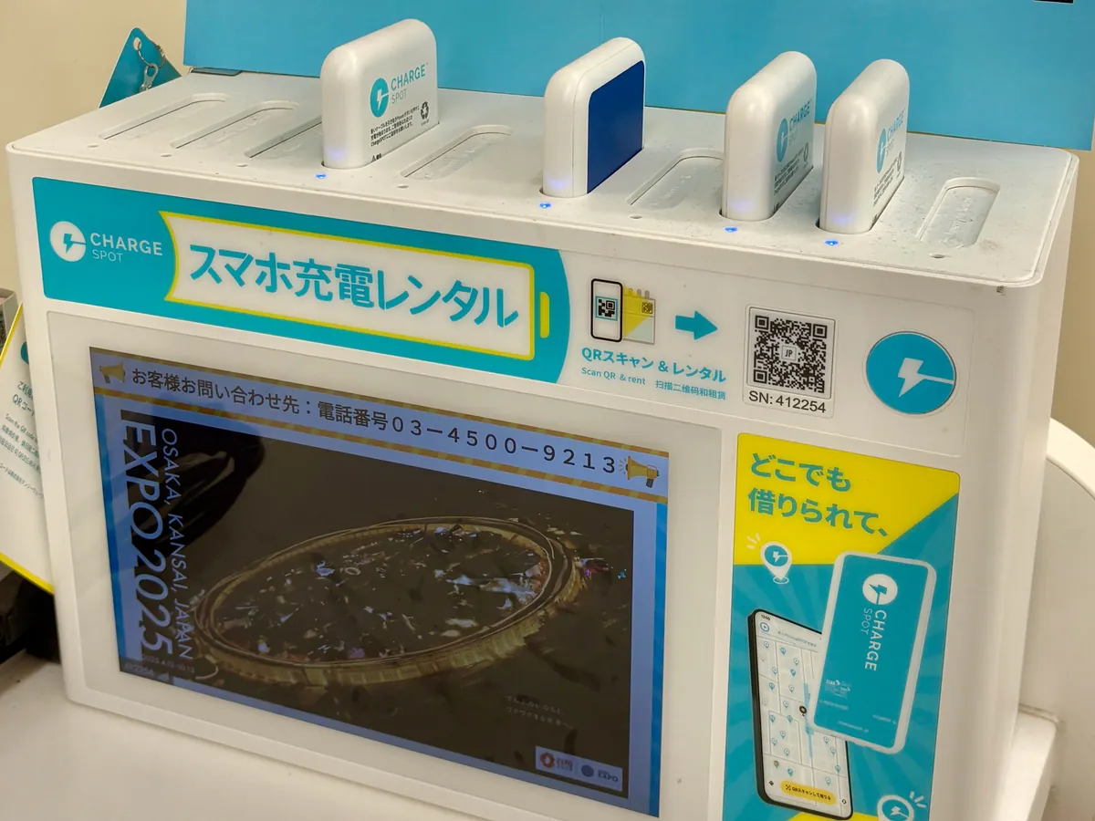 CHARGESPOTのバッテリースタンド。上部のスロットに白いバッテリーが4本差さり、正面の「スマホ充電レンタル」の表示の右にQRコードがある