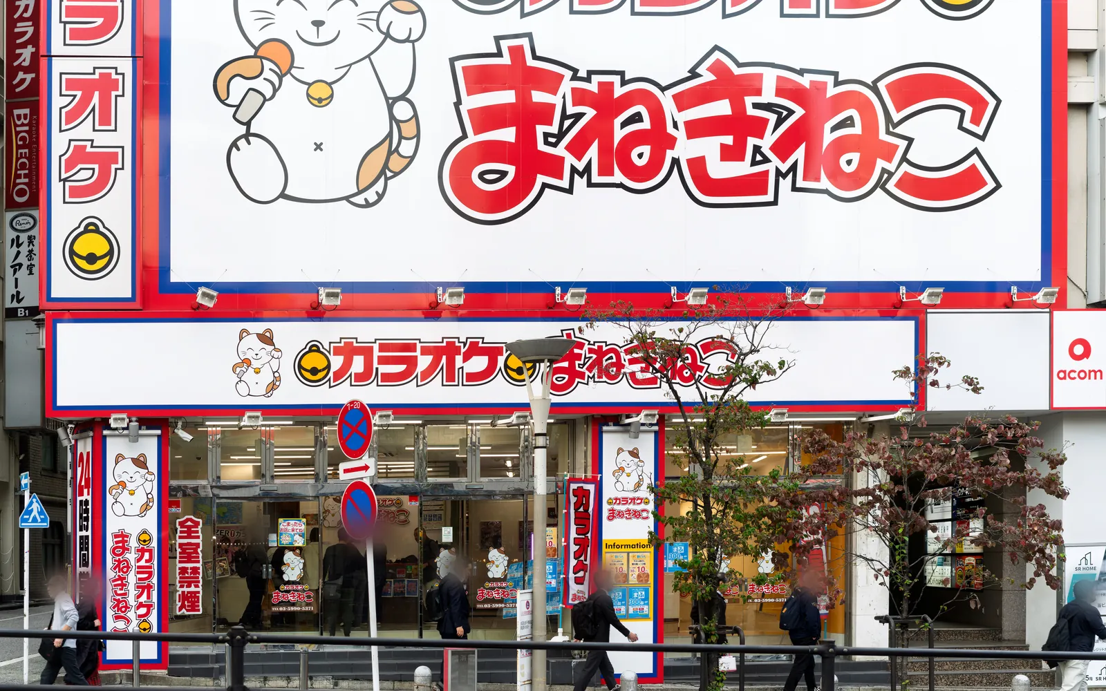 カラオケまねきねこ 新宿西口店の外観。招き猫のキャラクターと「カラオケ まねきねこ」の大きな看板の下に、ガラス張りの入口がある
