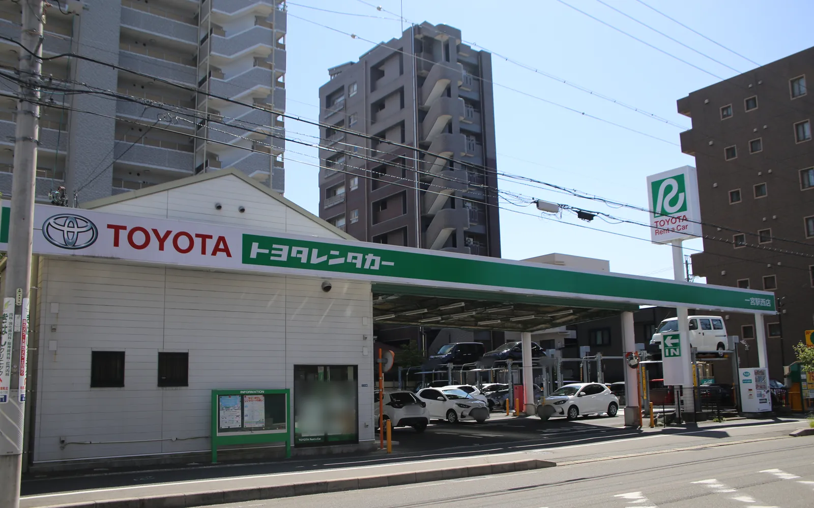 トヨタレンタカー 一宮駅西店の外観。「TOYOTA トヨタレンタカー」の看板の下に受付の建物と、貸し出し用の車が並ぶ駐車場がある